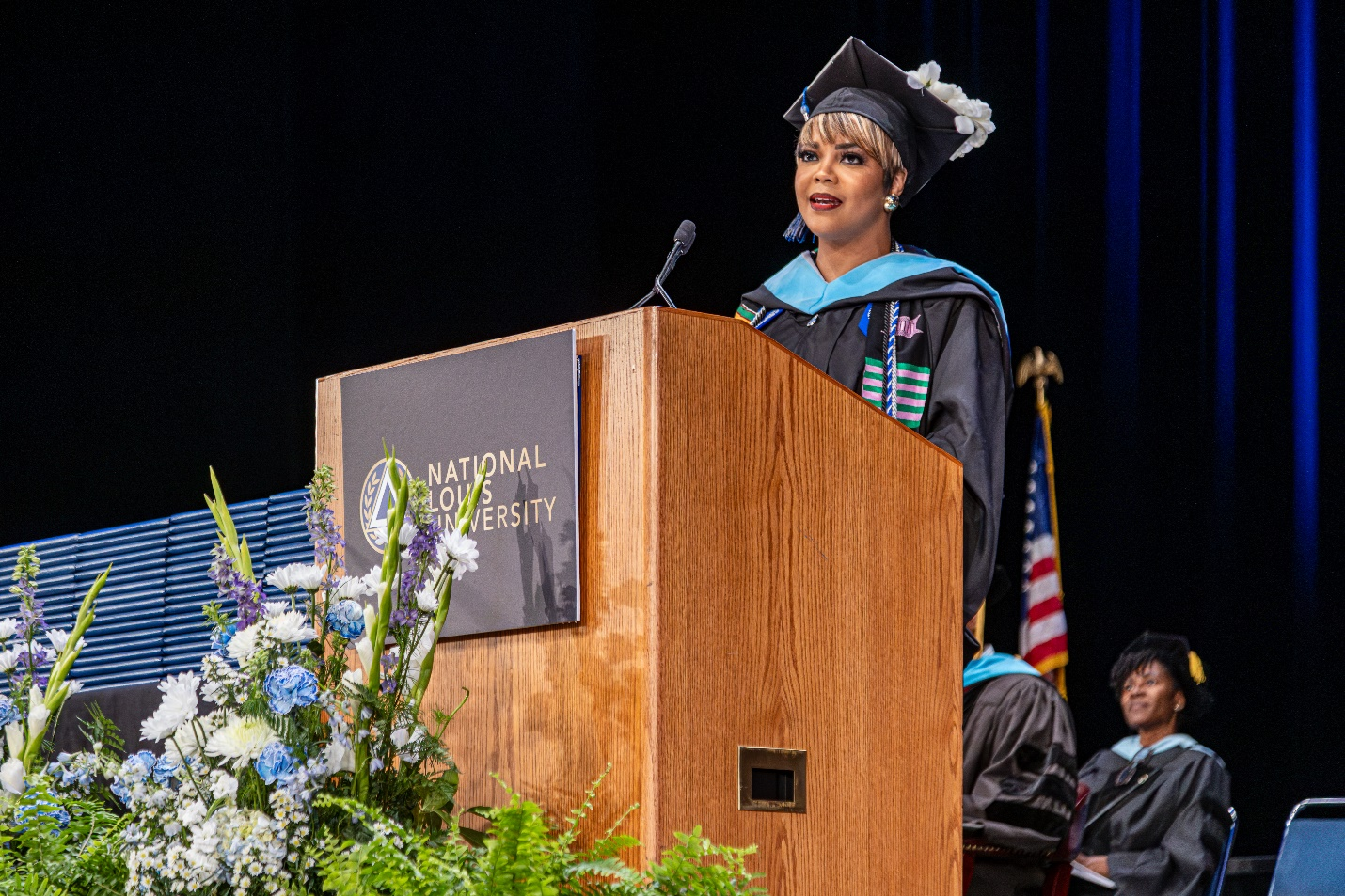 A student in graduation regalia speaking at a podium